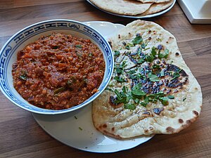 Eine kleine Schüssel Daal Curry auf einem Teller mit einem Naan, dass mit Koriander bestreut ist